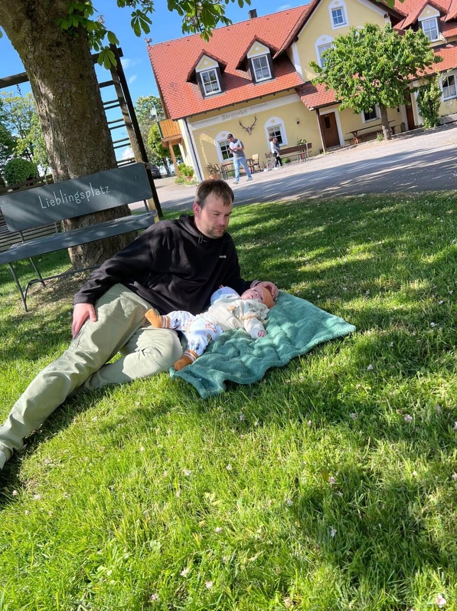 Papa mit Baby auf der Wiese vor dem Ferienhaus